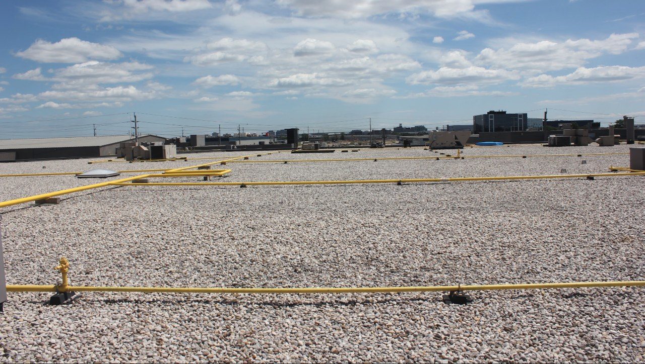 A gas line running across a ballasted flat roof field toward the parapet edge.