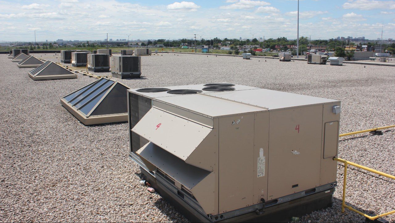 A rooftop mechanical unit in the foreground of a large ballasted flat roof, with skylights behind it.