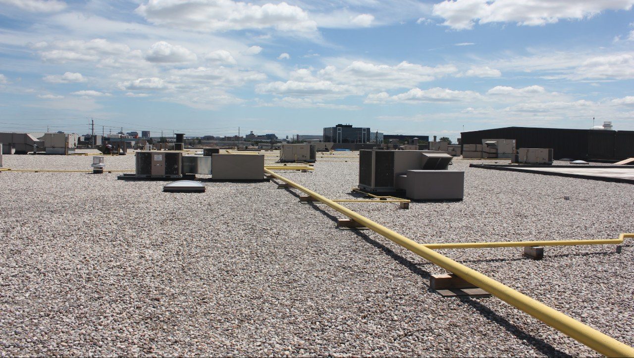 A row of rooftop mechanical units across a ballasted commercial flat roof.